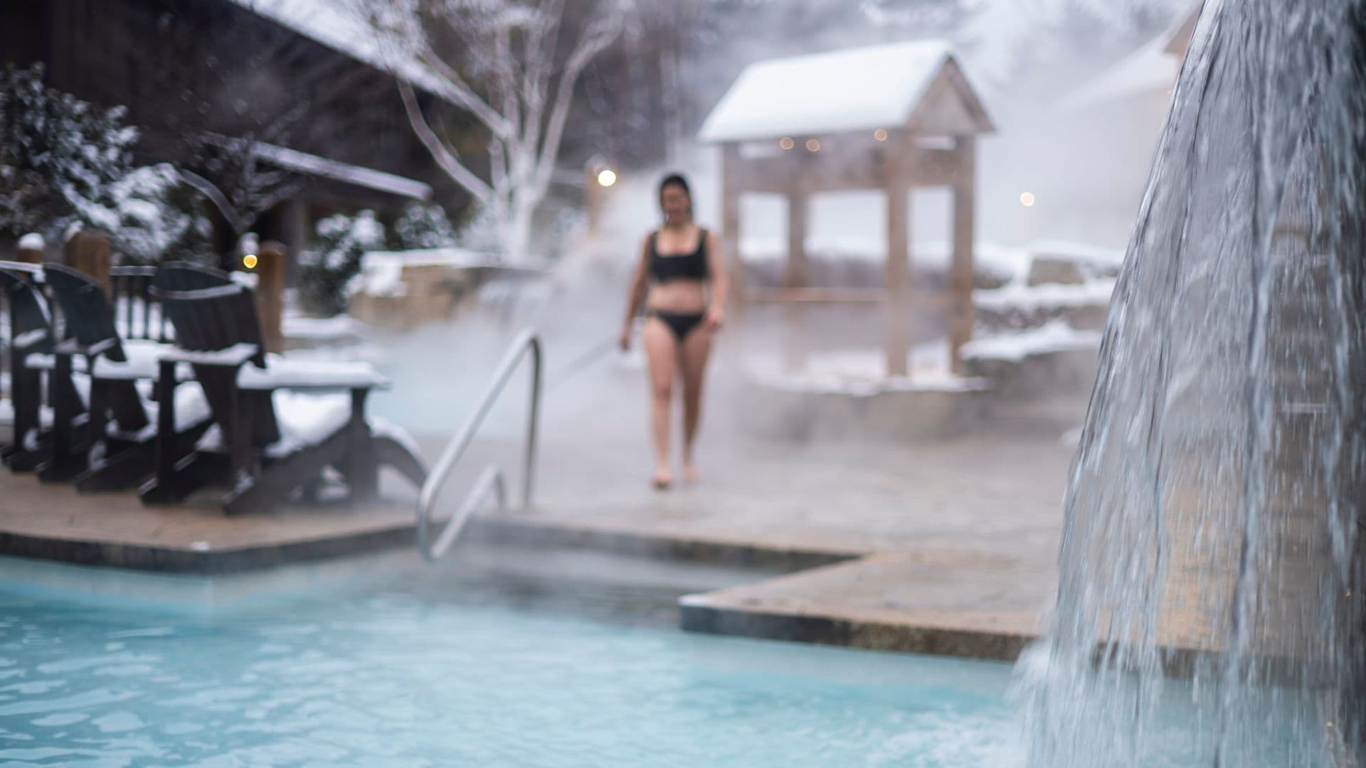 Guest walking toward a steaming outdoor thermal pool at Scandinave Spa Blue Mountain in winter